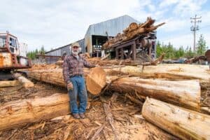 A man standing next to logs in a processing facility.