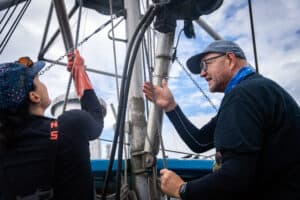 A man and woman speaking to one another as they work on a boat's lines.