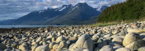 A large group of rocks on the beach with mountains in the background.