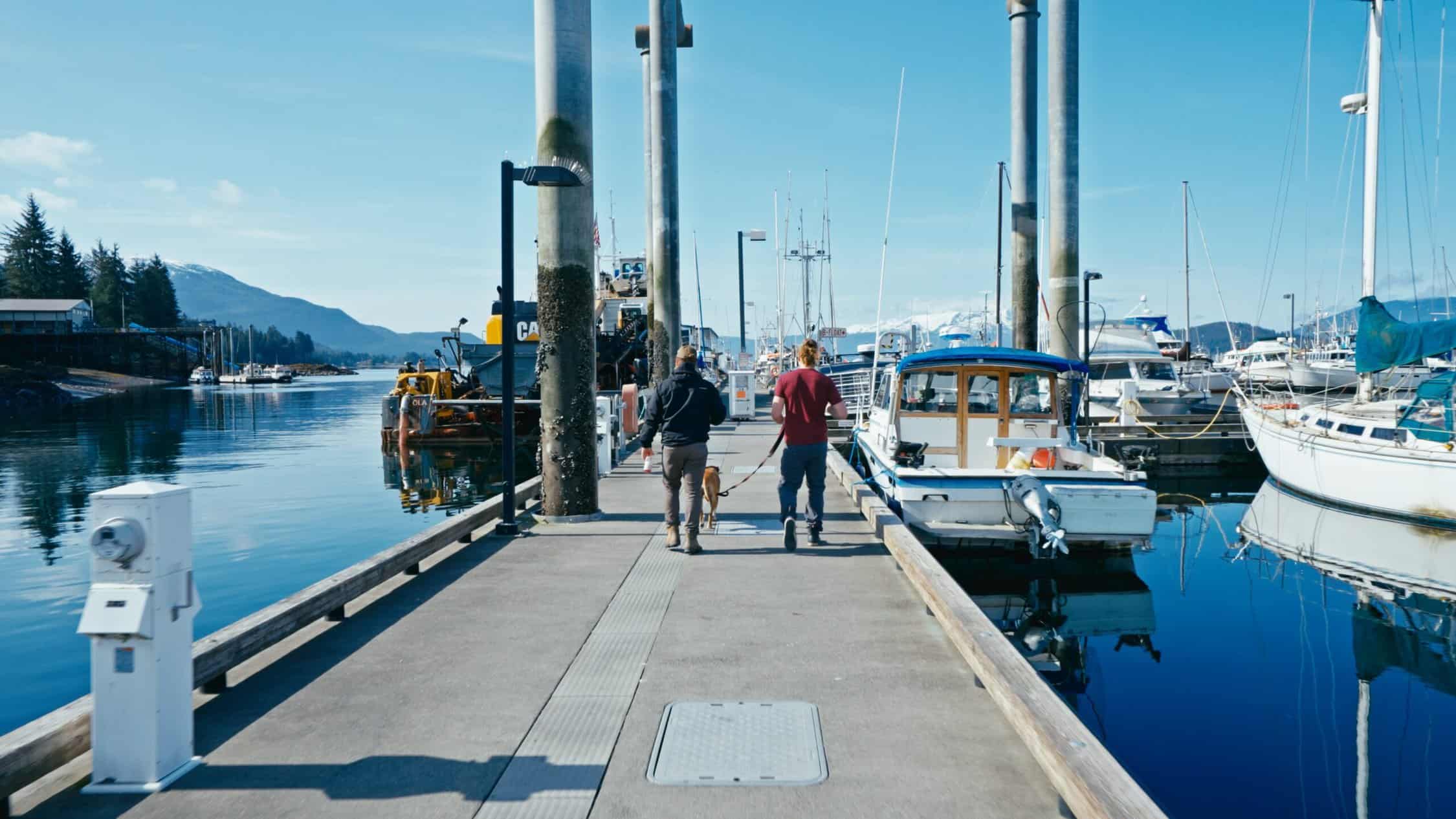 Two people walking on a dock near boats.